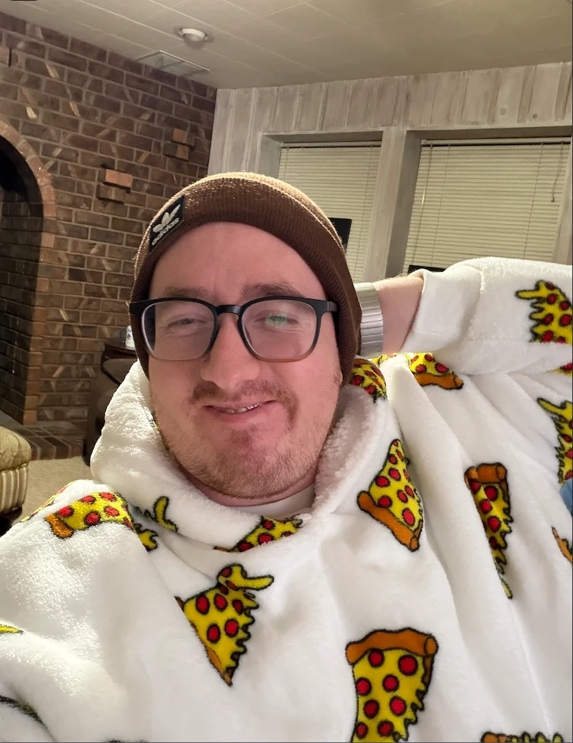 Cam wearing glasses and a beanie, wrapped in a pizza-print blanket.